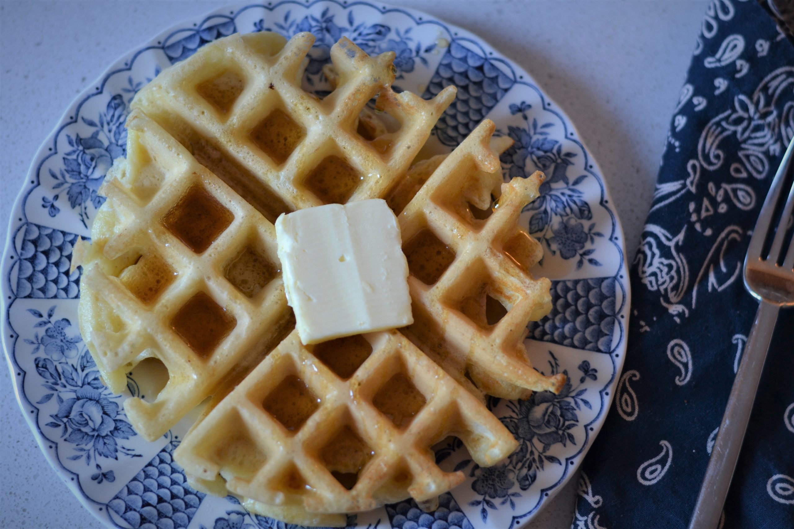 thick sourdough waffle with butter and syrup on a white and blue china plate